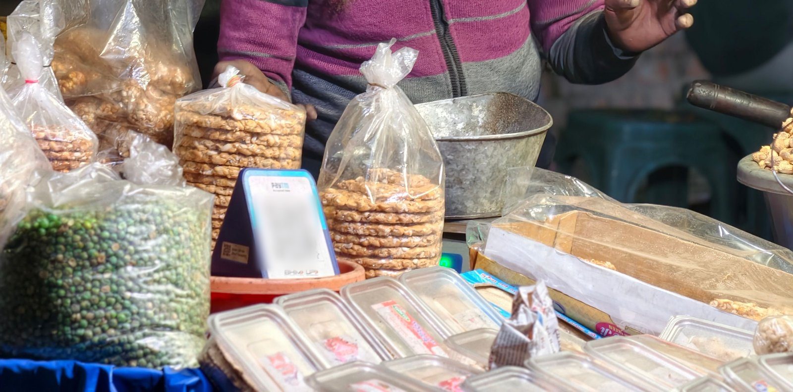 A street vendor's stall at a Delhi night market, with a UPI QR code stand among the snacks